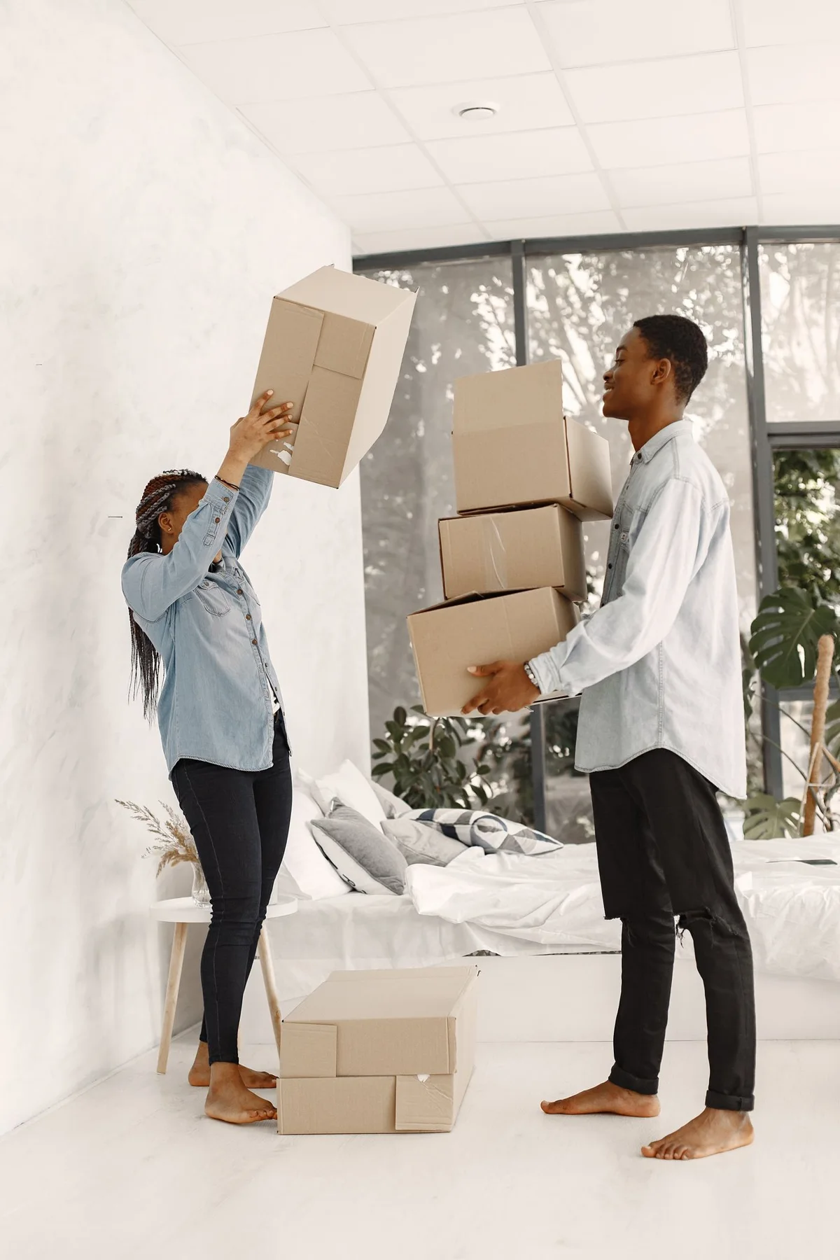 Two people holding moving boxes in a bedroom.