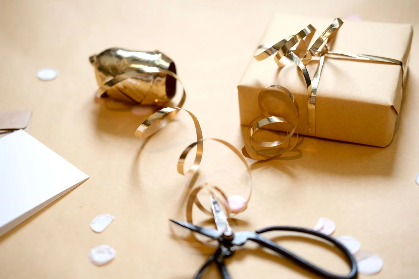 Brown-paper gift wrapping with gold ribbon and scissors on a table.
