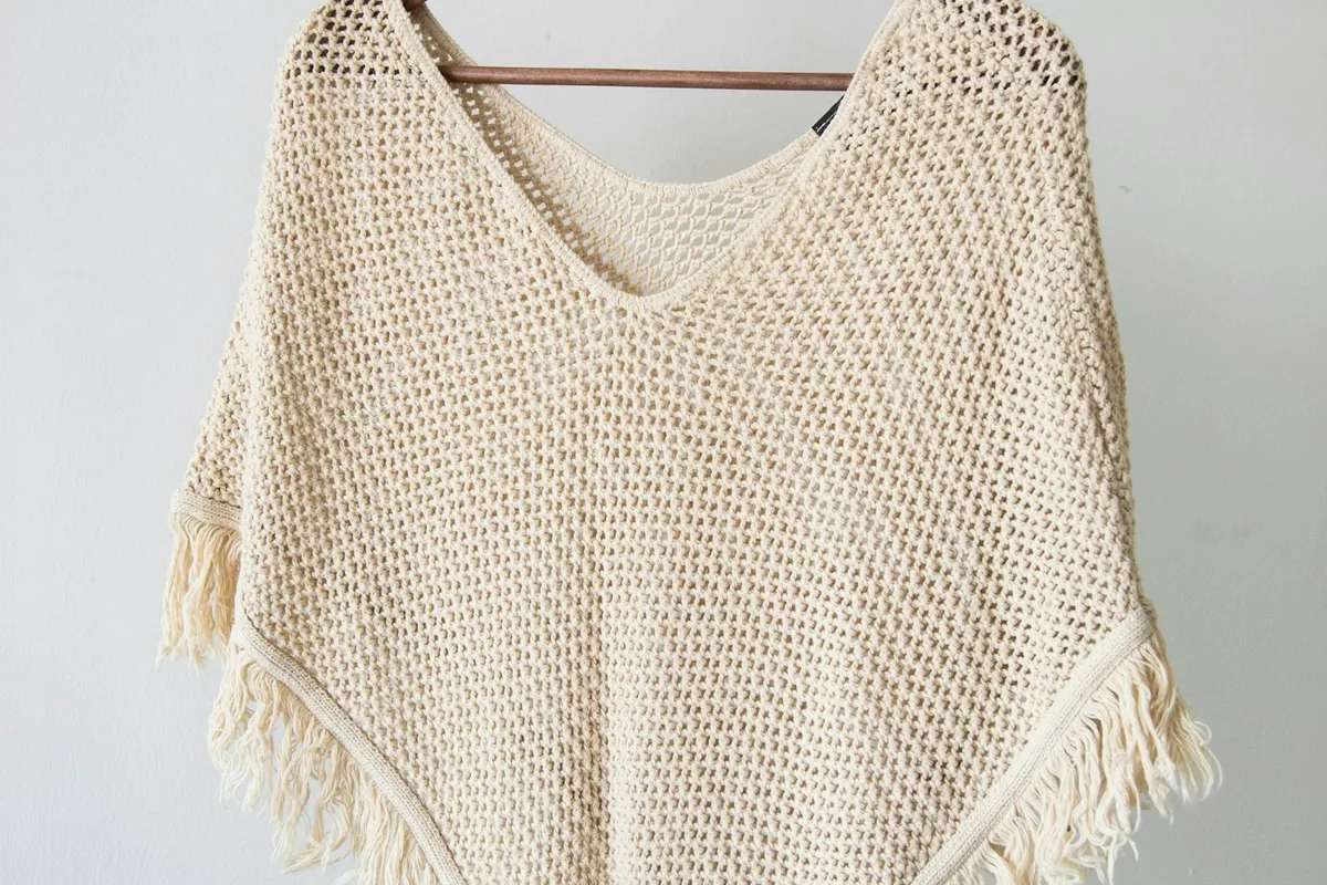 A pale open-textured knit garment on a wooden hanger.