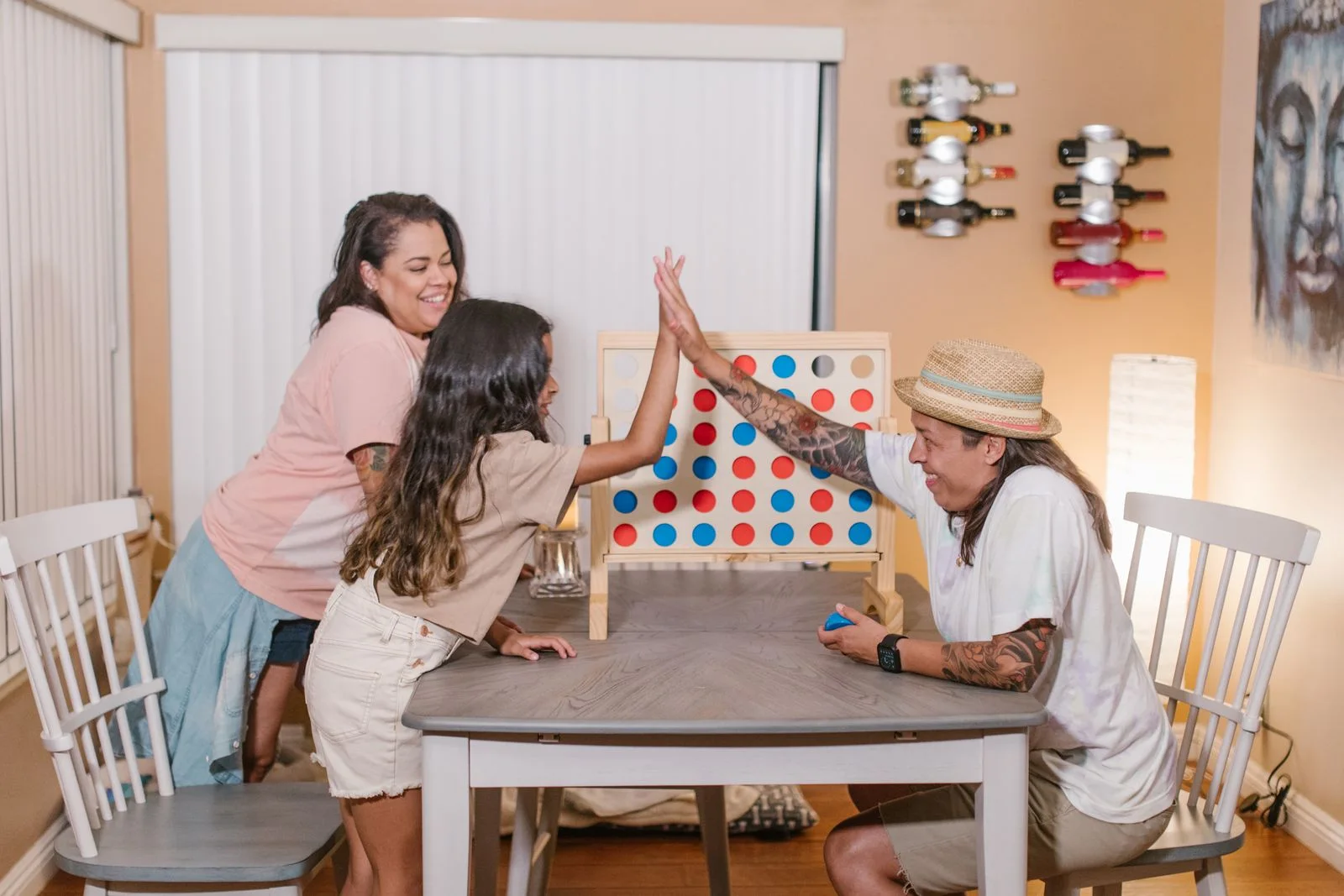 Three people gathered around a colourful upright board game on a wooden table.