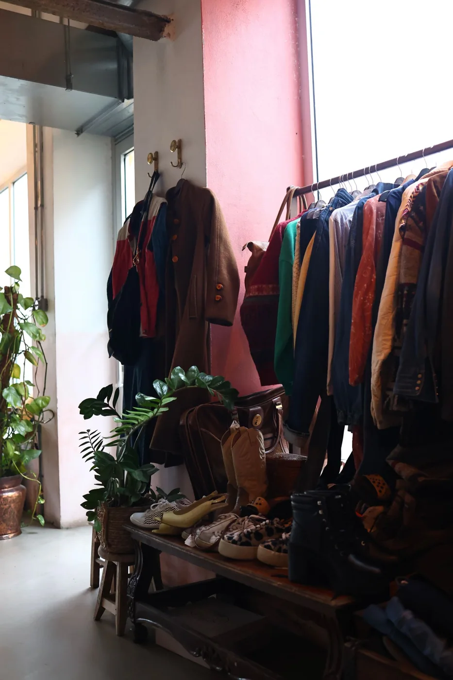 Coats on a rail and assorted belongings in a shop with a bright window.