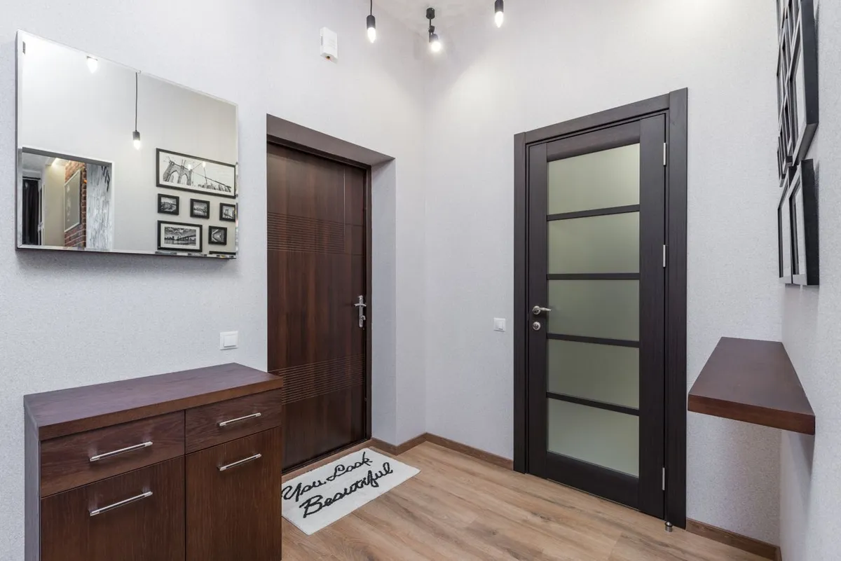 An entryway with dark wooden doors, a low cabinet and a mirror reflecting framed pictures.
