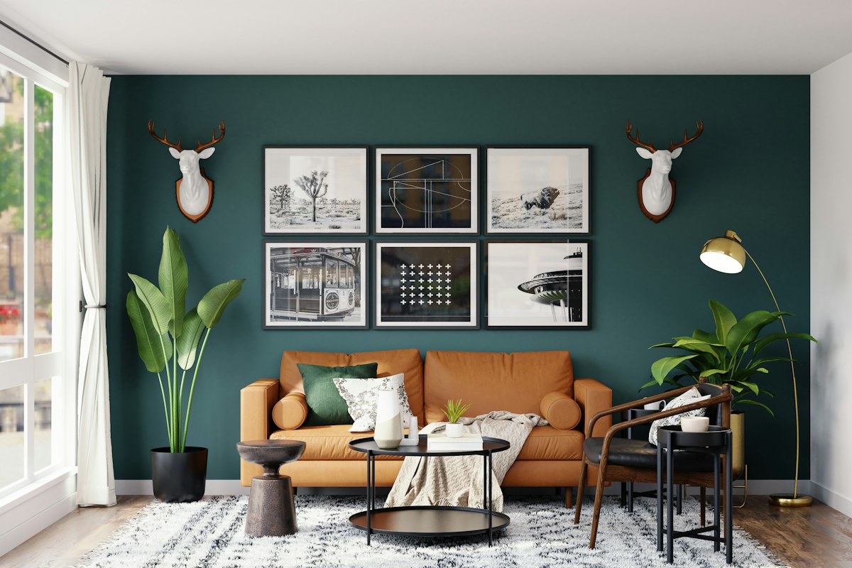 A tan sofa beneath framed pictures and decorative wall-mounted heads on a dark green wall.