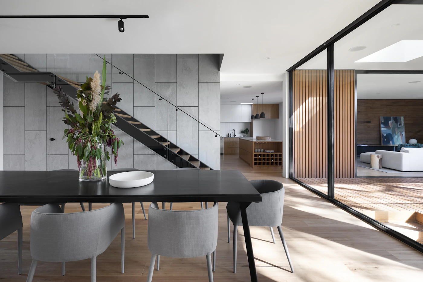 A dark dining table and chairs beside stairs and glazed doors in an open interior.