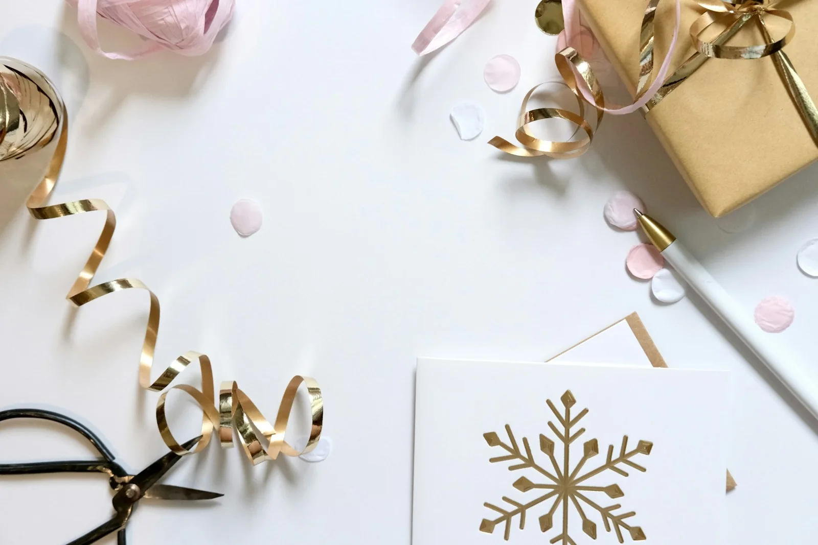 Pale wrapping paper, scissors, gold ribbon and a snowflake-design card on a light surface.