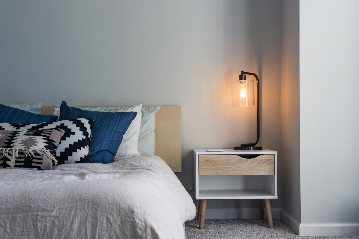 A bedside lamp beside pale bedding and blue patterned cushions.