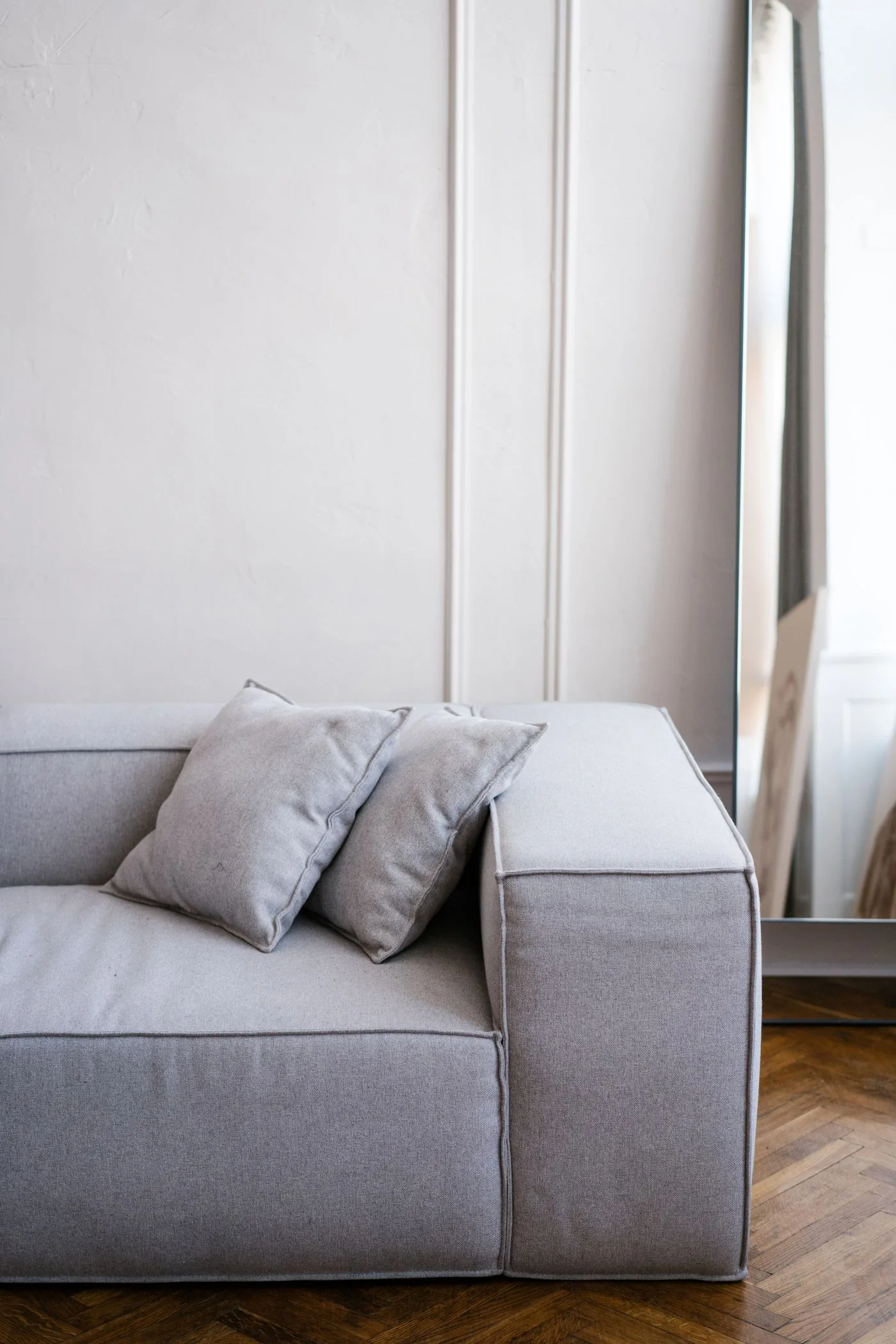 A grey sofa with pale cushions beside long curtains and a wall mirror.