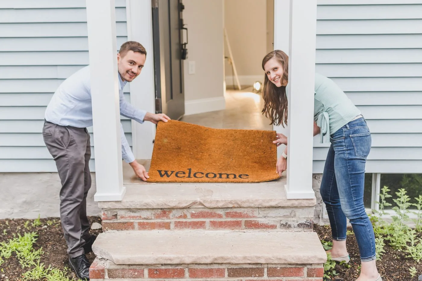 Two people holding a welcome mat at a front door.