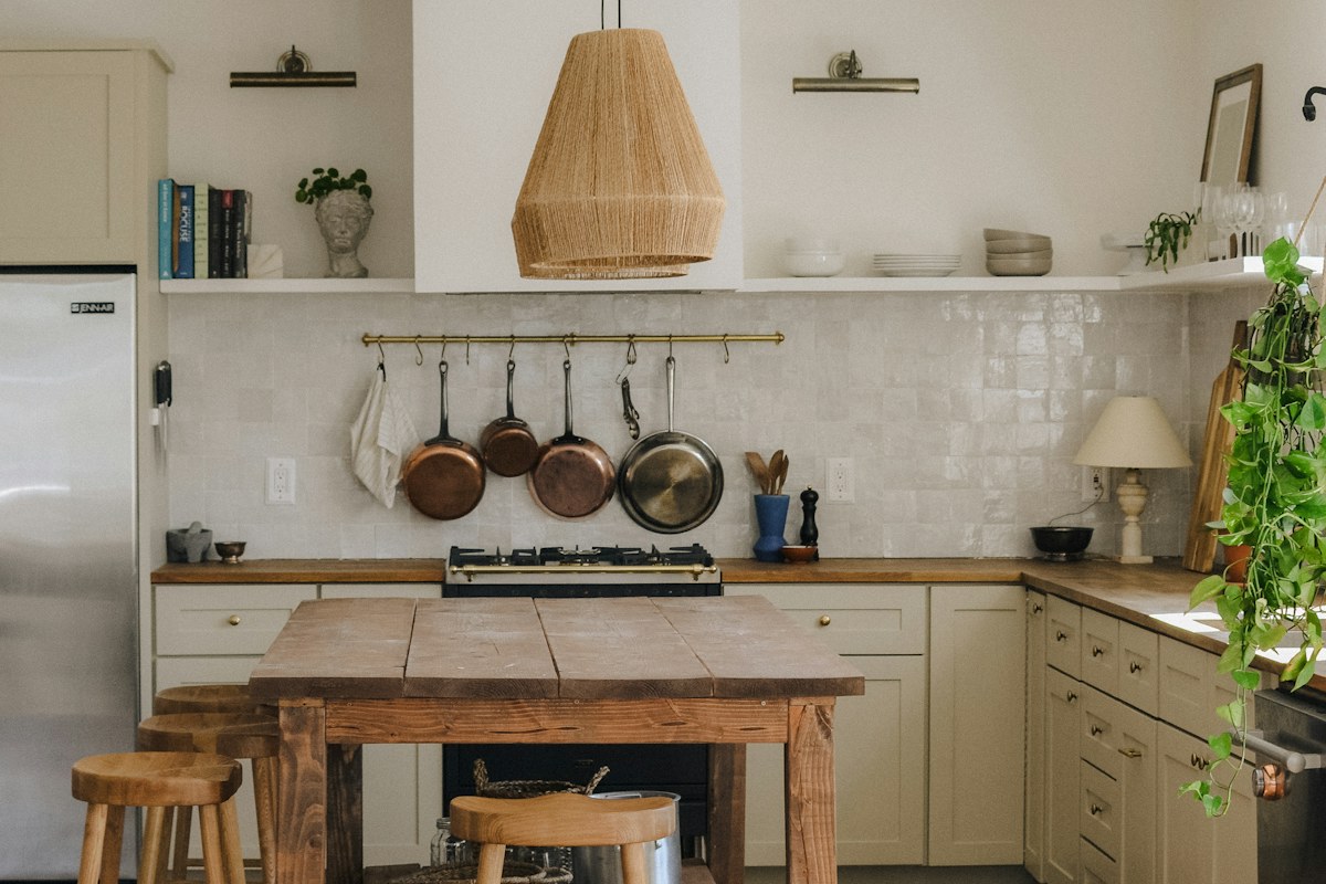 A kitchen with a wooden worktable, stools and hanging pans.