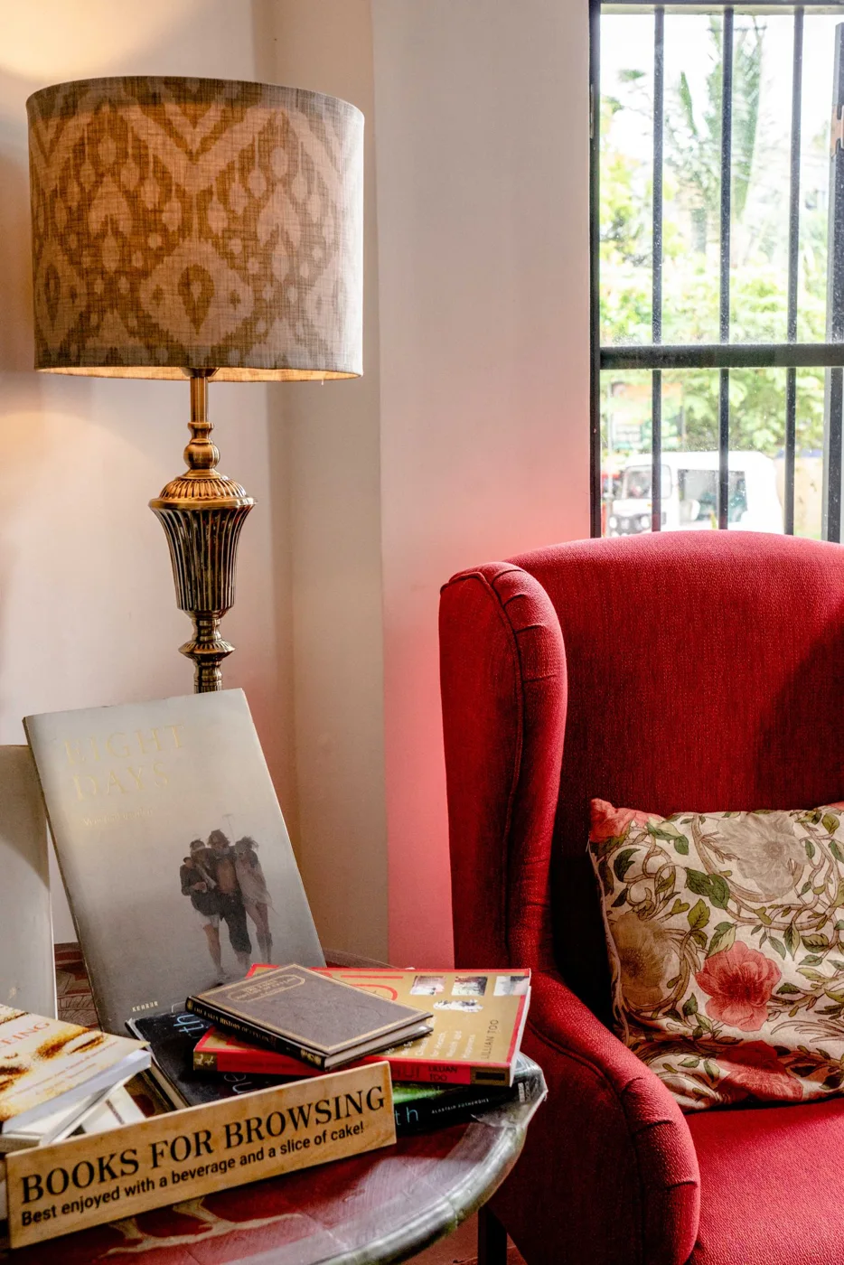 A red armchair beside a lamp and a table of books.