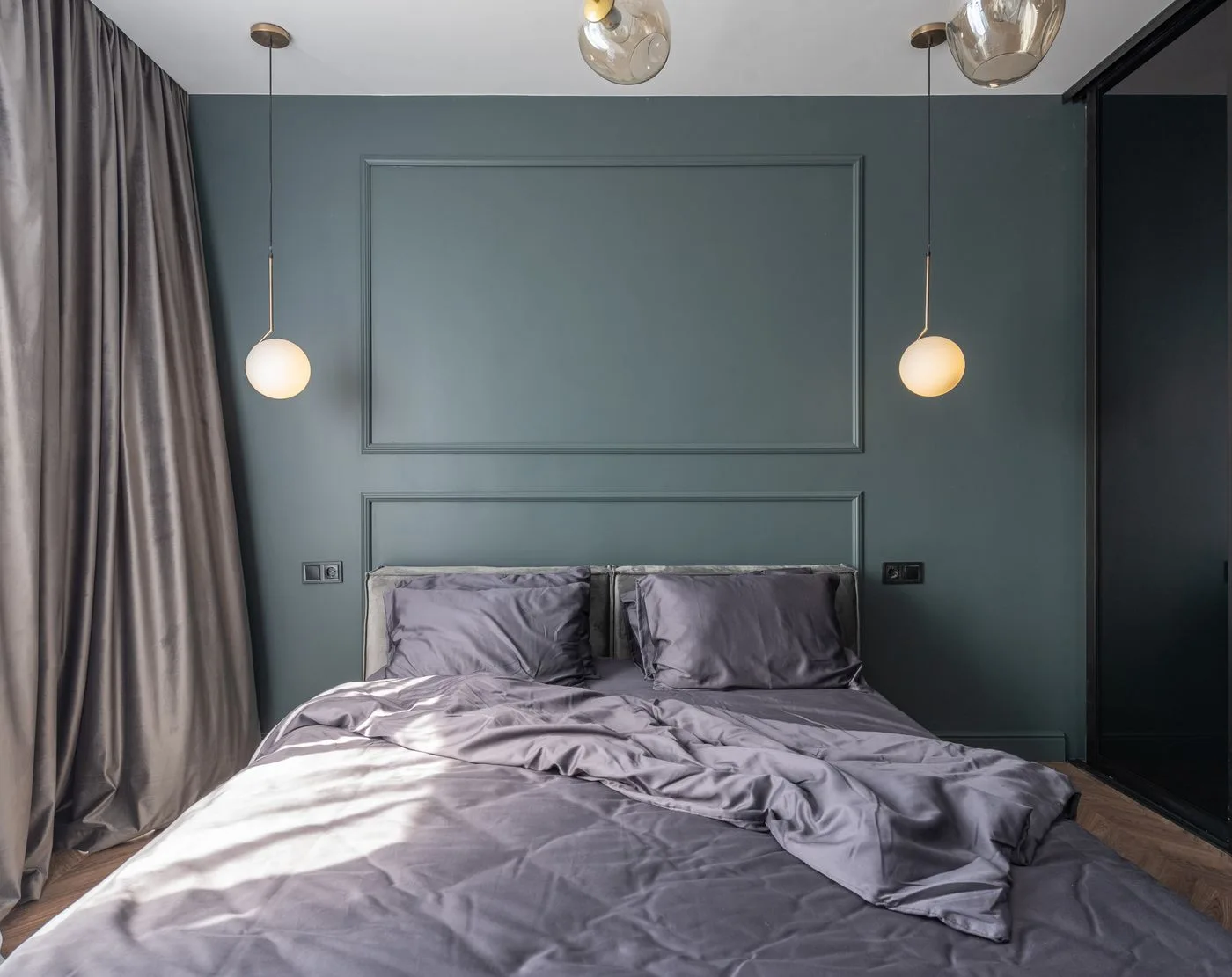 A dark blue bedroom with a bed and two hanging bedside lights.