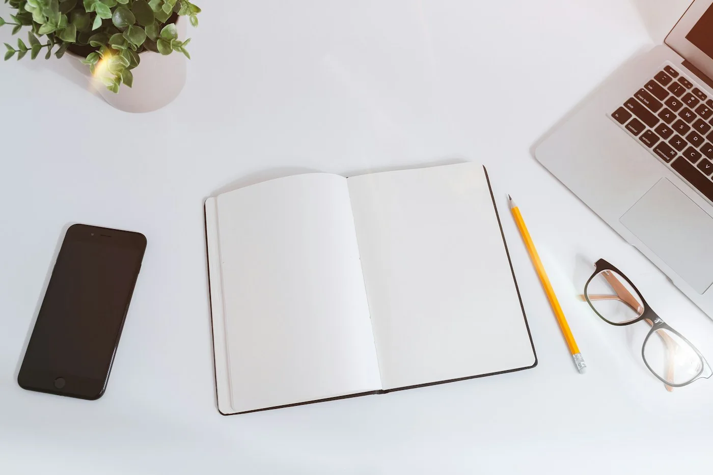 An open notebook beside a phone, glasses and writing tools.