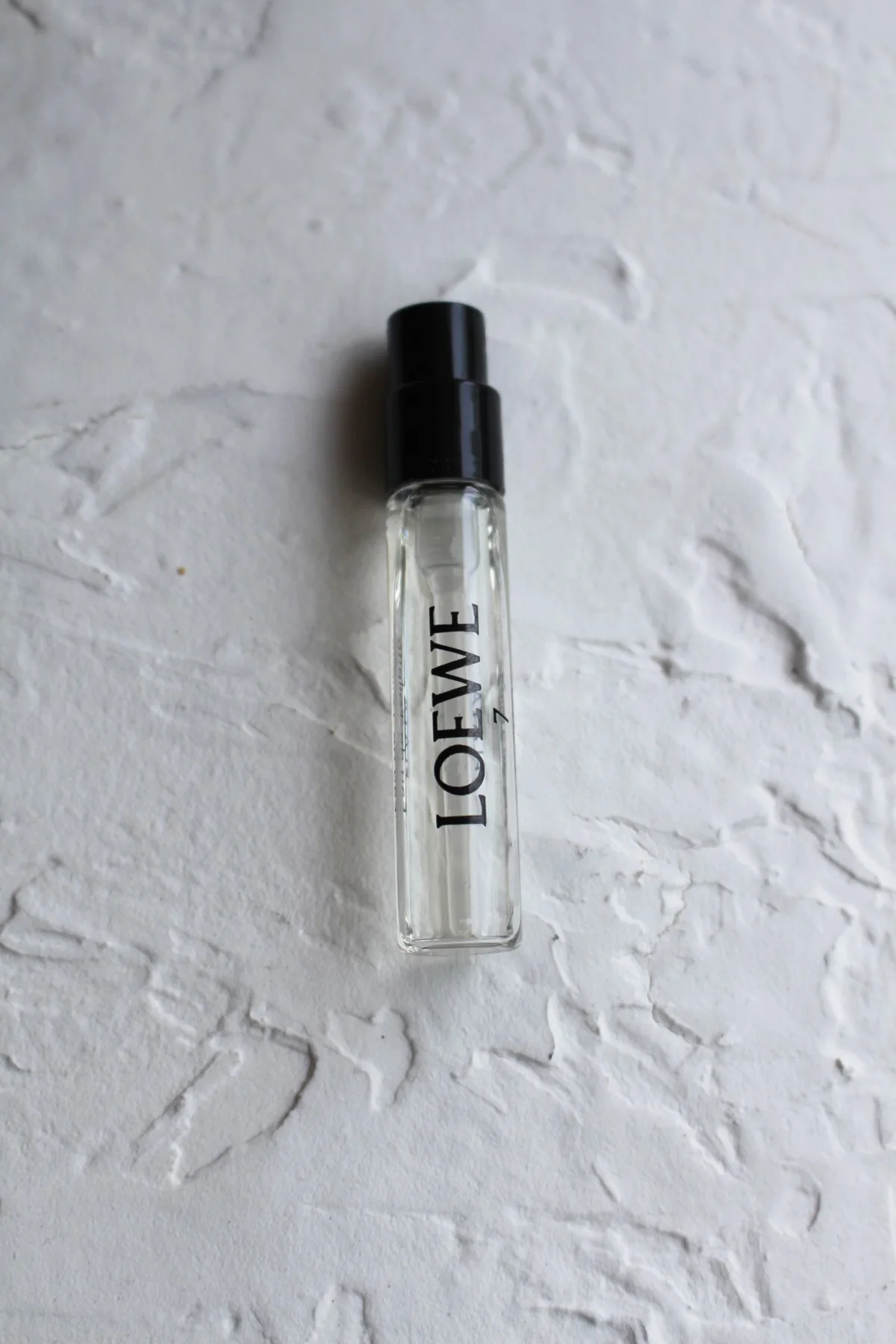 A labelled fragrance sample vial on a pale surface.
