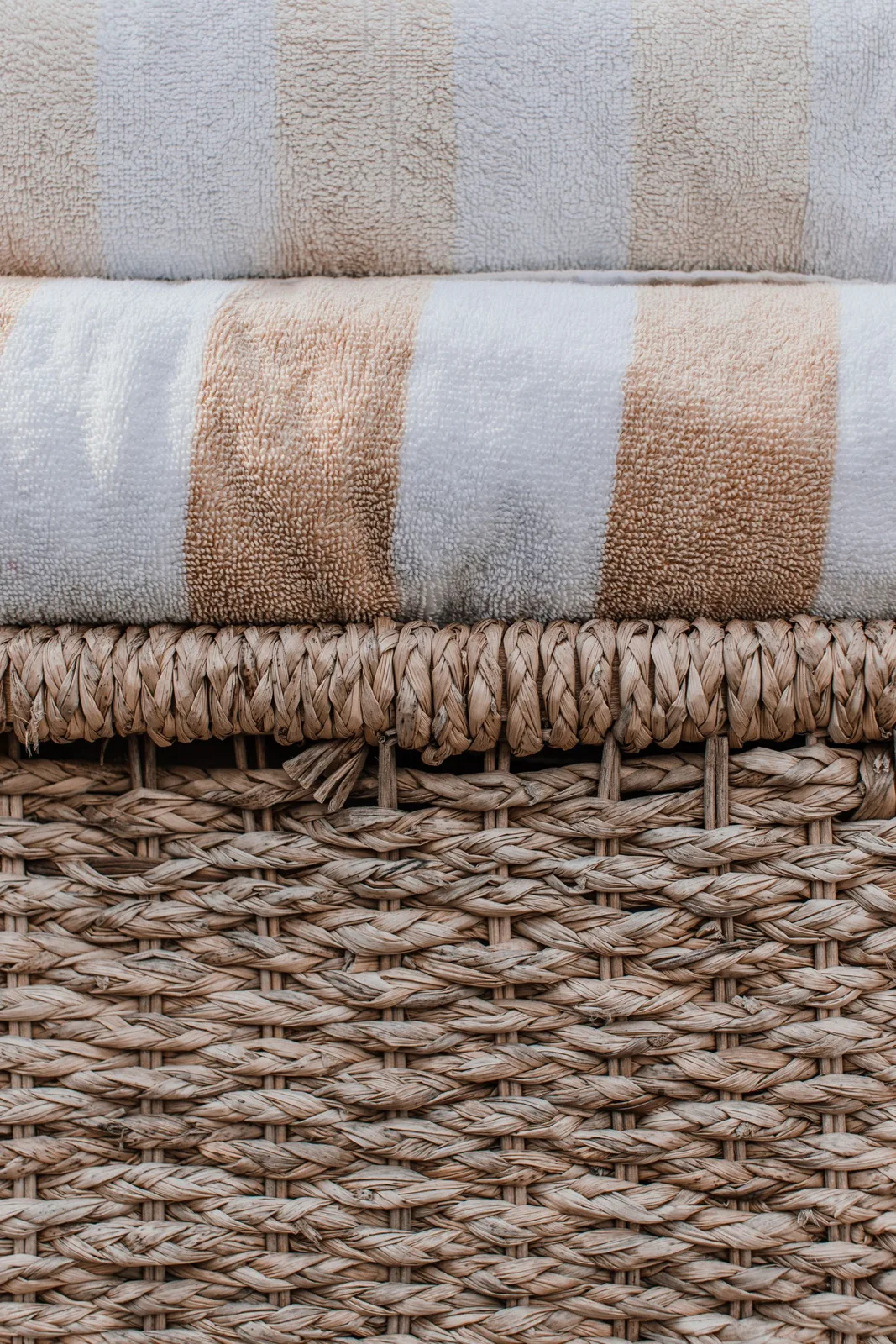 Folded striped towels resting on a woven basket.